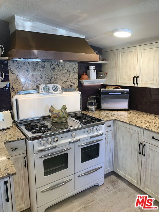 kitchen featuring range hood, decorative backsplash, double oven range, light hardwood / wood-style floors, and light stone countertops