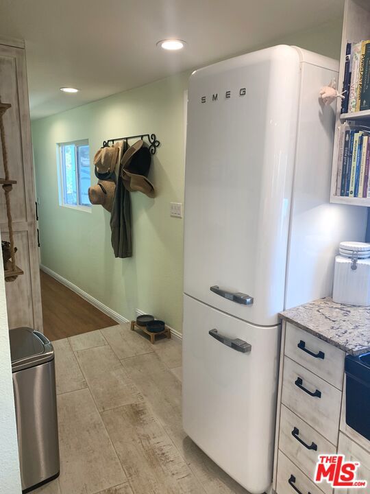 kitchen with white fridge, light wood-type flooring, light stone counters, and stove