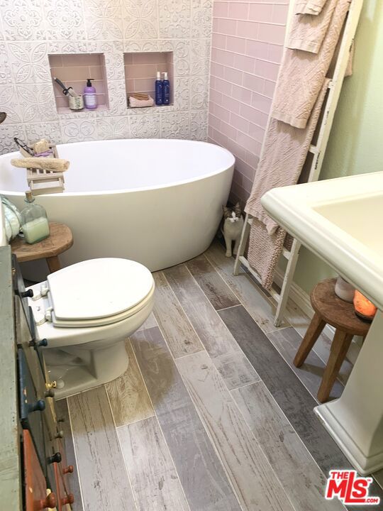 bathroom with a bathing tub, tile walls, and toilet