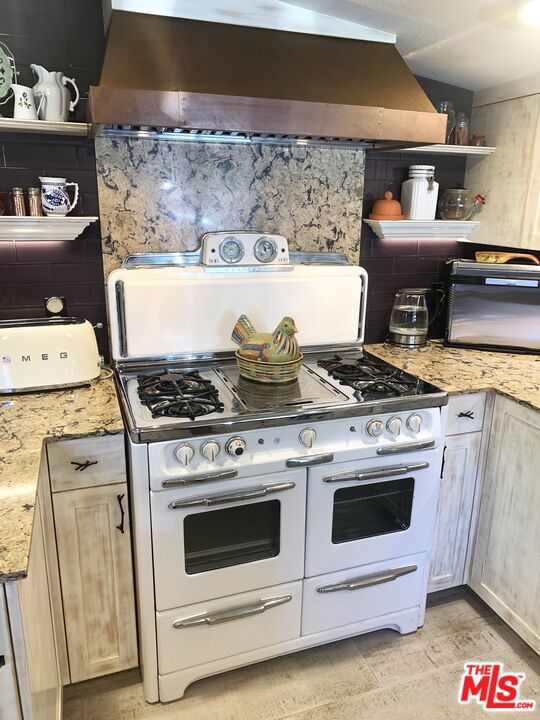 kitchen with range with two ovens, ventilation hood, backsplash, and light stone counters