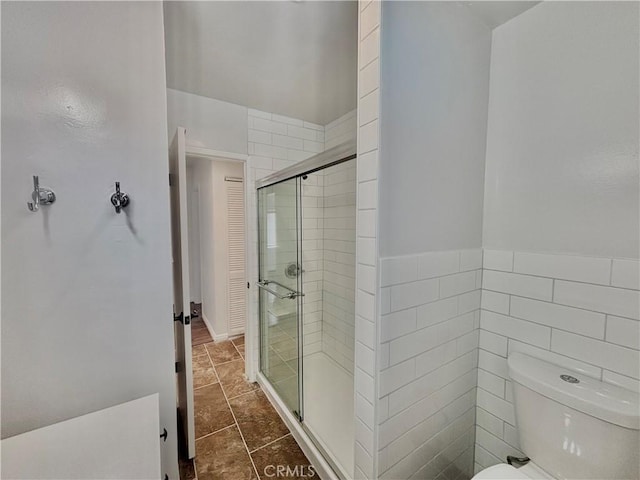 bathroom featuring tile patterned floors, toilet, a shower with shower door, and tile walls