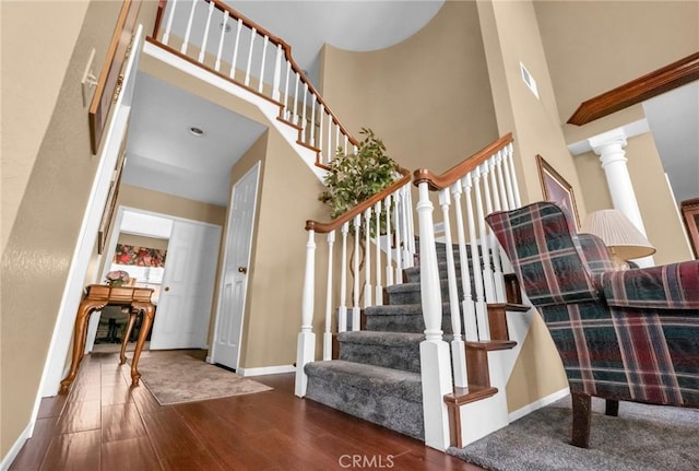 staircase with ornate columns, hardwood / wood-style floors, and a high ceiling