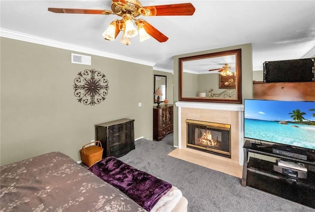 carpeted bedroom featuring ceiling fan, crown molding, and a tile fireplace