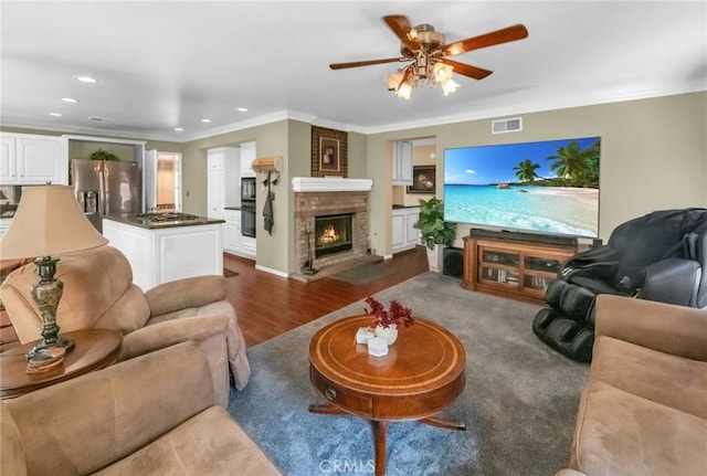 living room featuring a fireplace, hardwood / wood-style floors, ceiling fan, and crown molding