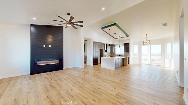 unfurnished living room featuring ceiling fan, a large fireplace, light wood-type flooring, and high vaulted ceiling