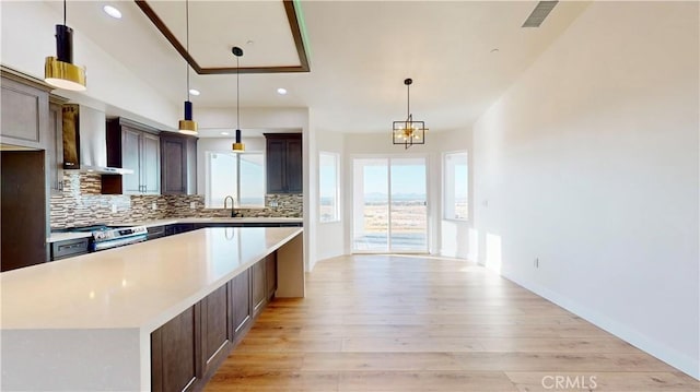 kitchen featuring light hardwood / wood-style floors, a kitchen island, hanging light fixtures, and wall chimney range hood