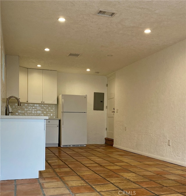 kitchen with white refrigerator, electric panel, sink, white cabinets, and backsplash