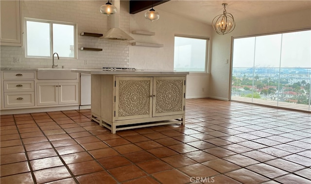 kitchen with vaulted ceiling with beams, hanging light fixtures, sink, a kitchen island, and decorative backsplash