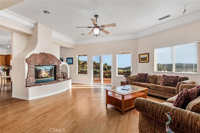 living room with ceiling fan, light wood-type flooring, a fireplace, and ornamental molding