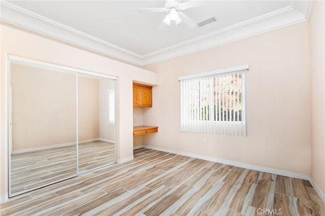 unfurnished bedroom with ceiling fan, built in desk, light wood-type flooring, and a closet