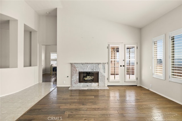 unfurnished living room featuring a fireplace, french doors, high vaulted ceiling, and dark wood-type flooring