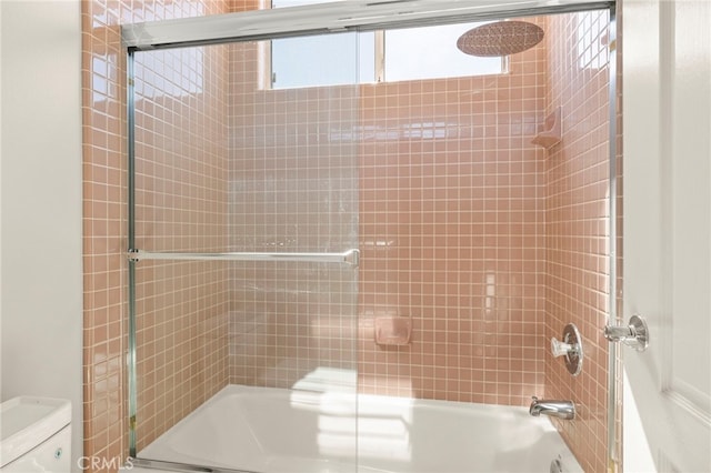 bathroom featuring toilet and shower / bath combination with glass door