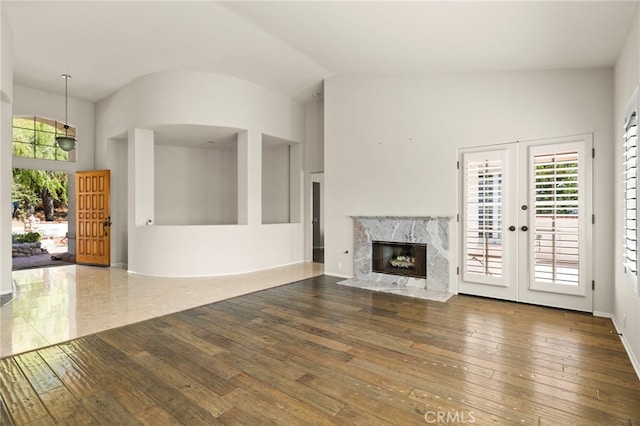 unfurnished living room featuring french doors, a high end fireplace, wood-type flooring, and high vaulted ceiling