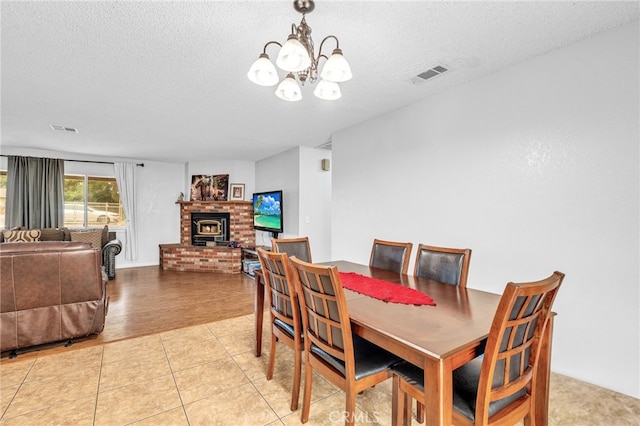 dining room with light hardwood / wood-style floors, a textured ceiling, a fireplace, and a notable chandelier