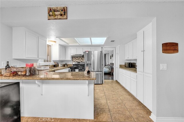 kitchen with white cabinets, kitchen peninsula, appliances with stainless steel finishes, and stone counters