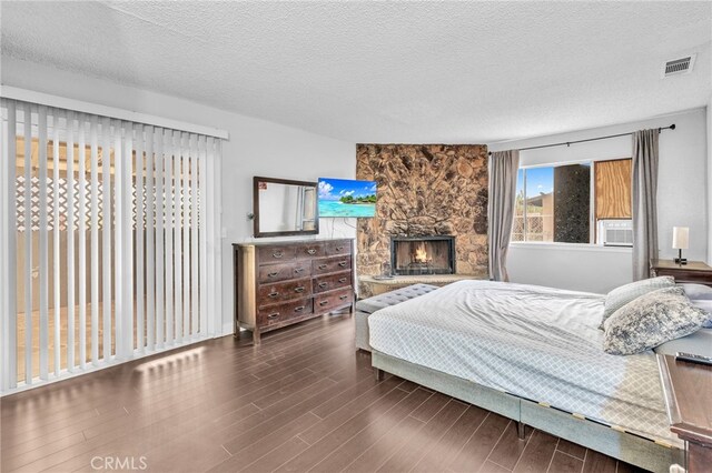 bedroom featuring a textured ceiling, a stone fireplace, and dark hardwood / wood-style flooring