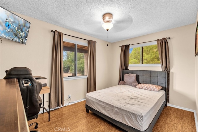 bedroom with a textured ceiling, wood-type flooring, and ceiling fan