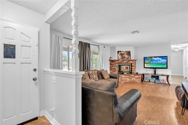 living room featuring a brick fireplace, a textured ceiling, and light hardwood / wood-style floors