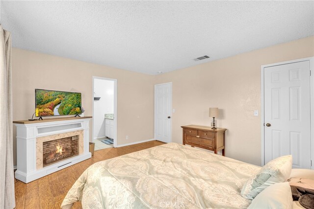 bedroom with light wood-type flooring, a textured ceiling, and ensuite bathroom