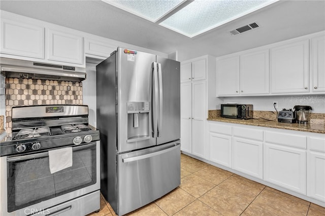 kitchen featuring dark stone countertops, white cabinetry, light tile patterned flooring, backsplash, and stainless steel appliances