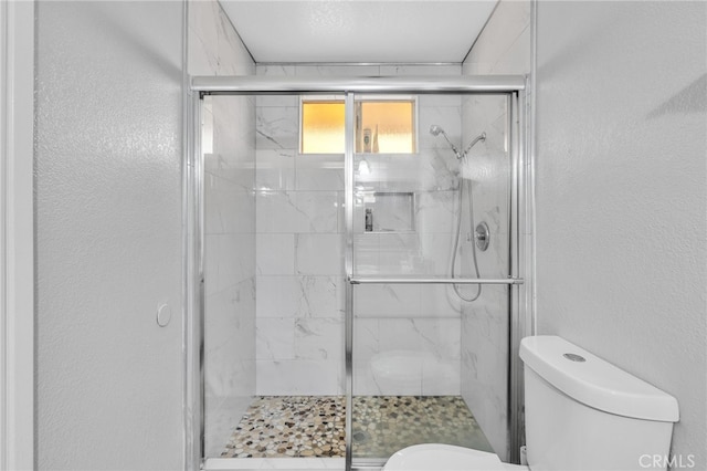 bathroom with a shower with shower door and toilet