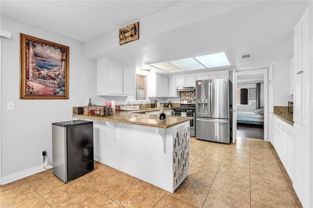 kitchen featuring white cabinets, kitchen peninsula, a textured ceiling, appliances with stainless steel finishes, and dark stone countertops