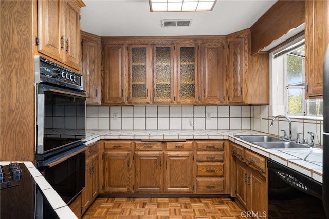 kitchen with backsplash, light parquet floors, black appliances, sink, and tile counters