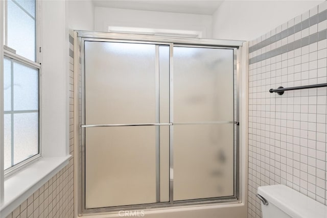 bathroom featuring toilet, a shower with shower door, and tile walls