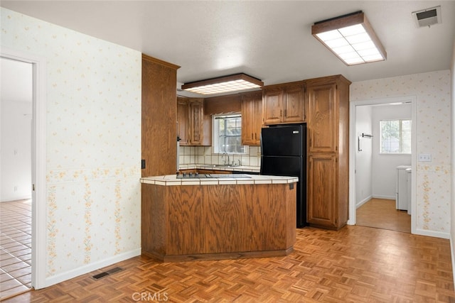 kitchen with light parquet flooring, black fridge, tile counters, and a healthy amount of sunlight