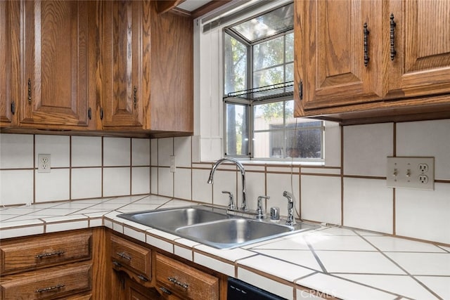 kitchen featuring backsplash, tile counters, sink, and dishwashing machine