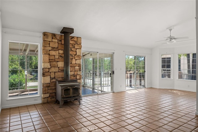 unfurnished living room with dark tile patterned flooring, ceiling fan, a wood stove, and a wealth of natural light