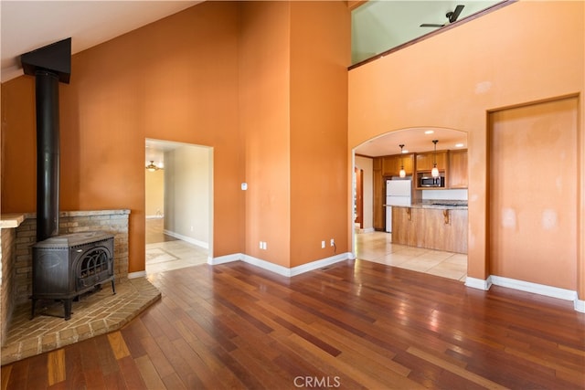 unfurnished living room with light hardwood / wood-style flooring, a high ceiling, a wood stove, and ceiling fan