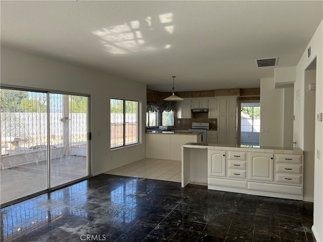 kitchen featuring a textured ceiling, white gas stove, white cabinetry, kitchen peninsula, and hanging light fixtures