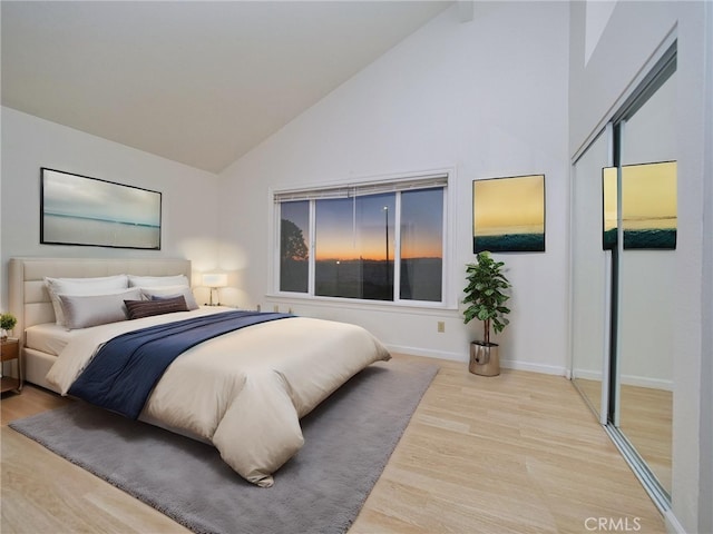 bedroom with high vaulted ceiling, light hardwood / wood-style floors, and a closet