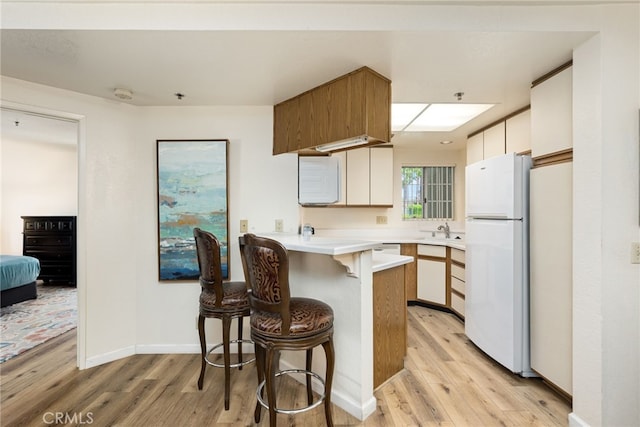 kitchen featuring a kitchen breakfast bar, white refrigerator, light hardwood / wood-style floors, and kitchen peninsula