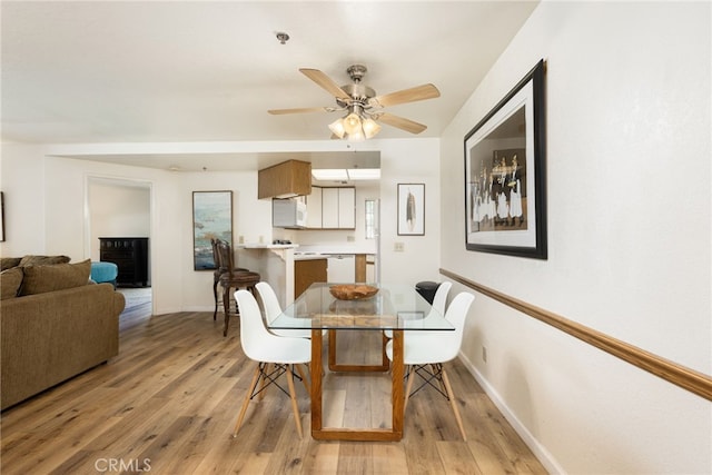 dining space with ceiling fan, light hardwood / wood-style floors, and a fireplace