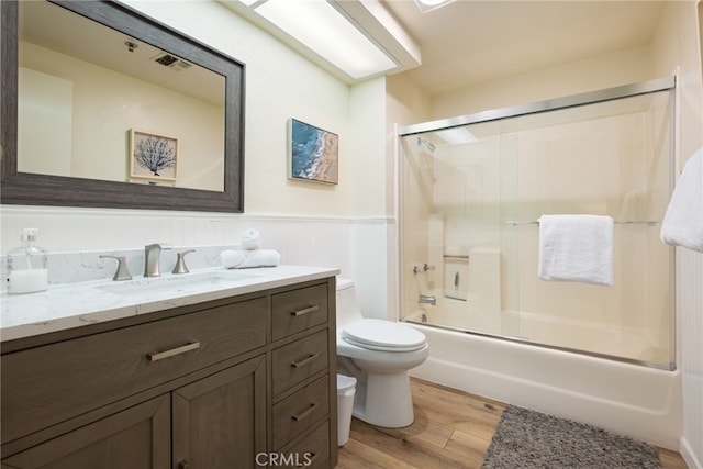 full bathroom featuring toilet, hardwood / wood-style floors, vanity, and combined bath / shower with glass door