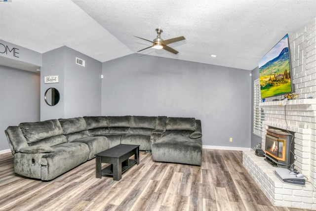 living room featuring vaulted ceiling, a fireplace, a wood stove, ceiling fan, and hardwood / wood-style floors