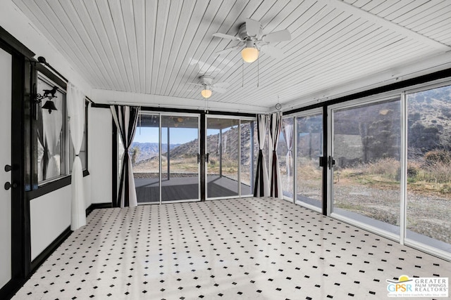 unfurnished sunroom featuring ceiling fan, a mountain view, and plenty of natural light