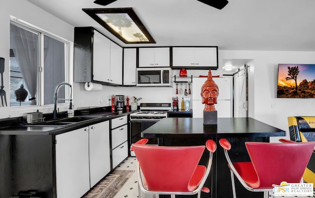 kitchen with sink, white cabinetry, a center island, white gas range, and a barn door