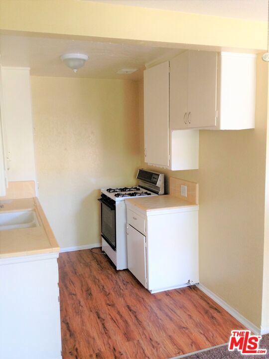 kitchen with white cabinets, white gas range oven, hardwood / wood-style flooring, and sink