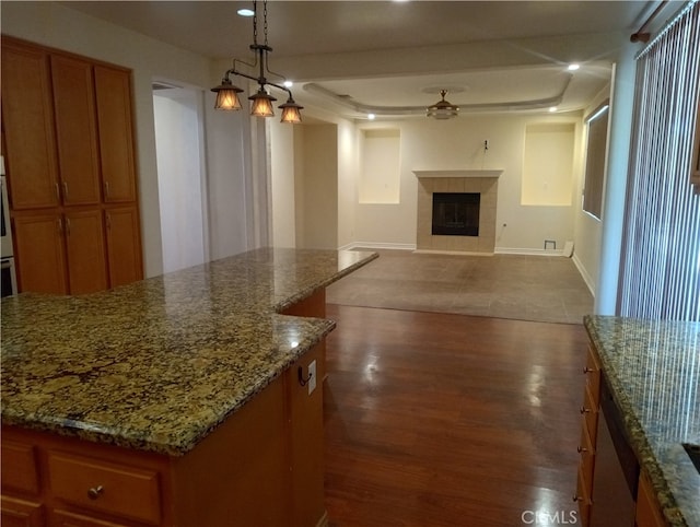 kitchen featuring a tile fireplace, wood-type flooring, a kitchen island, and decorative light fixtures