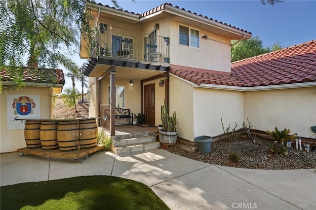 back of property with a tile roof, a balcony, and stucco siding