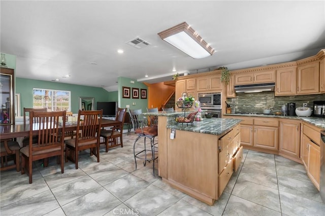 kitchen featuring visible vents, appliances with stainless steel finishes, a kitchen breakfast bar, under cabinet range hood, and backsplash