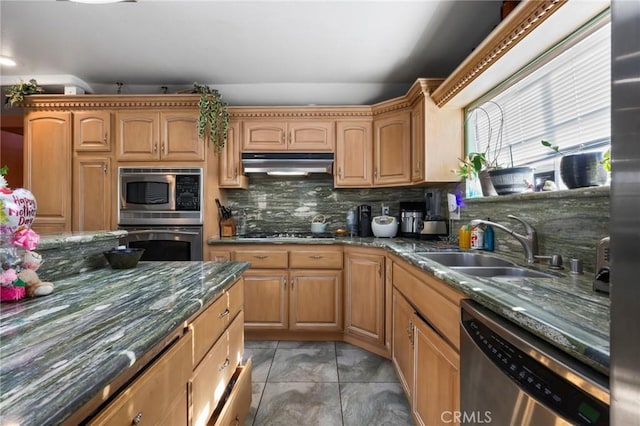 kitchen with stainless steel appliances, decorative backsplash, a sink, dark stone counters, and under cabinet range hood