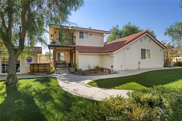 rear view of property featuring a balcony, a tile roof, a lawn, and stucco siding