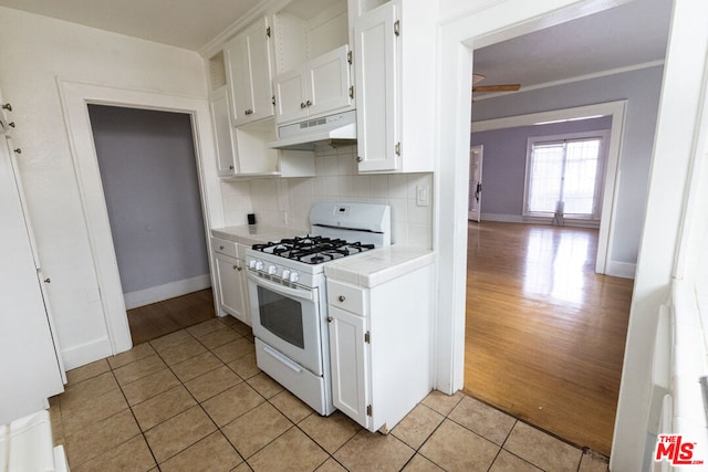 kitchen with white gas range oven, light hardwood / wood-style floors, decorative backsplash, white cabinets, and ornamental molding