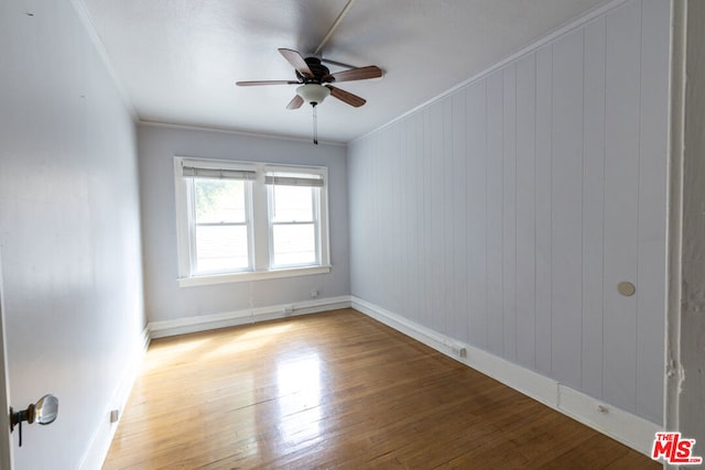 empty room with hardwood / wood-style floors, ceiling fan, ornamental molding, and wooden walls