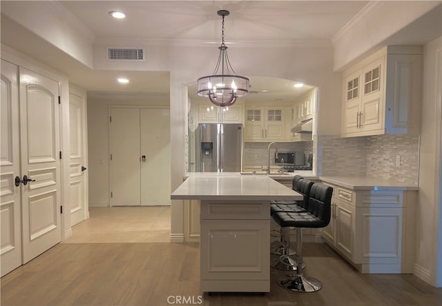 kitchen with light wood-type flooring, a center island, a kitchen bar, hanging light fixtures, and stainless steel fridge