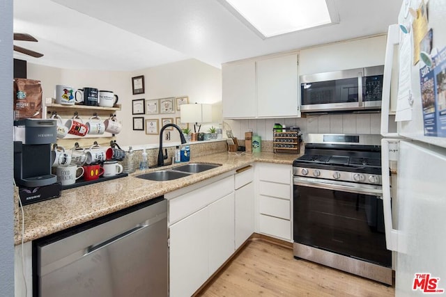 kitchen with white cabinets, stainless steel appliances, sink, and light hardwood / wood-style flooring